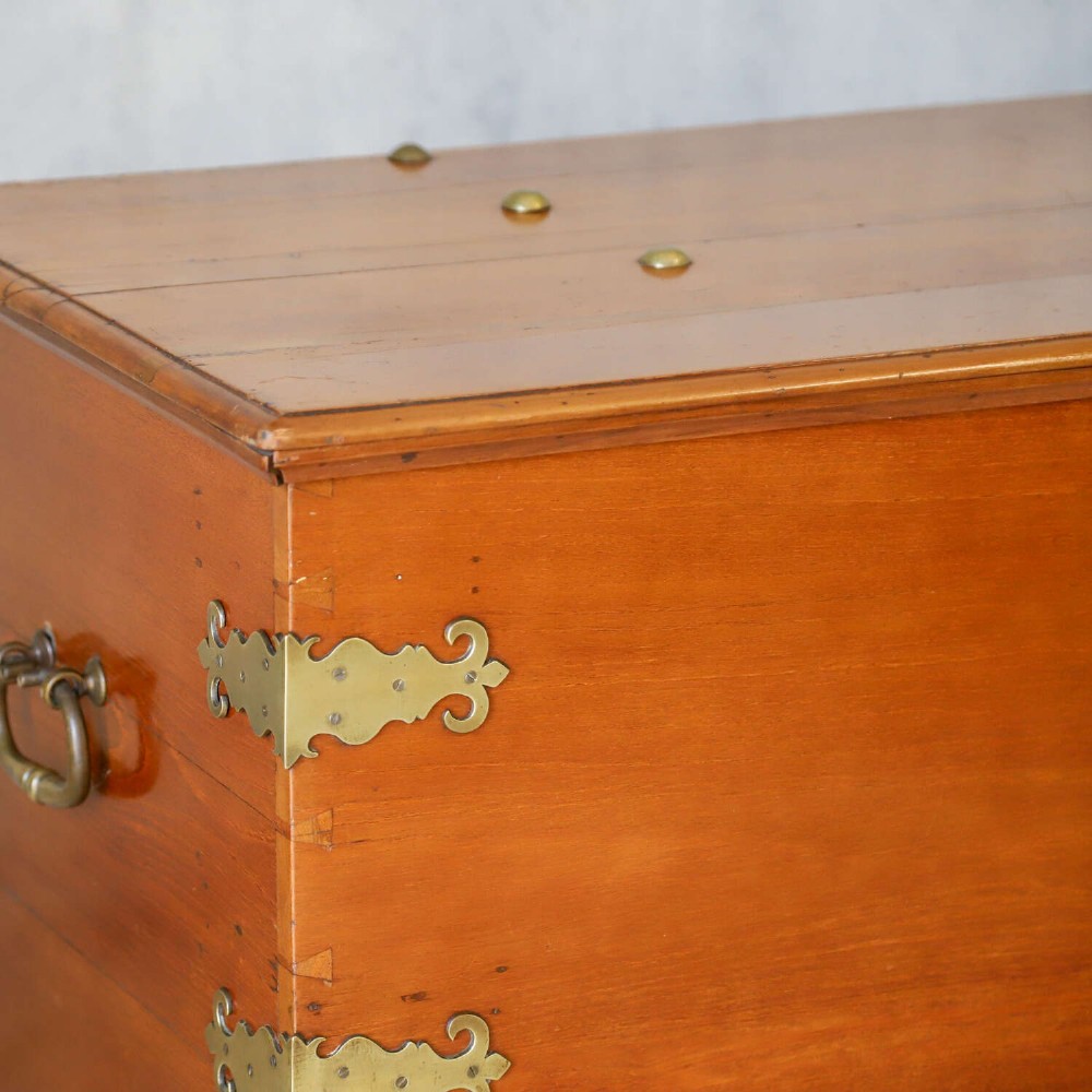 An 18th-century walnut colonial chest featuring decorative brass corner brackets, a central brass escutcheon, and dark turned feet. View V