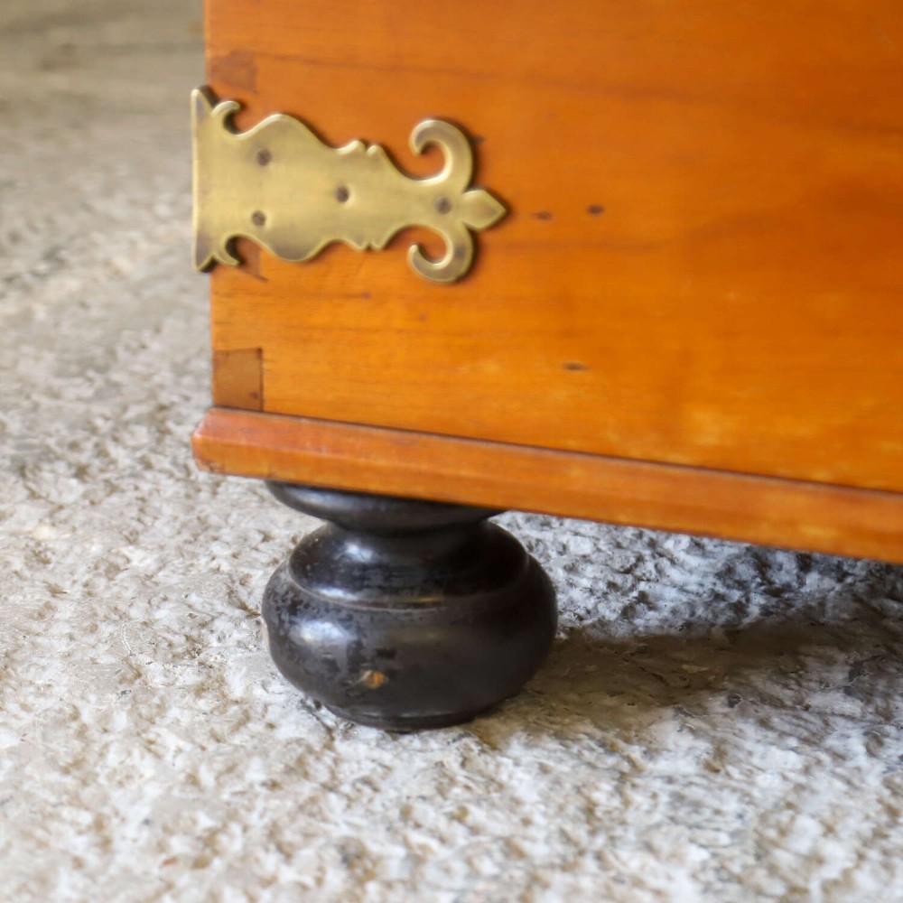An 18th-century walnut colonial chest featuring decorative brass corner brackets, a central brass escutcheon, and dark turned feet. View IX