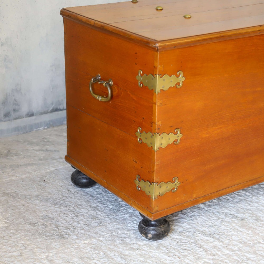 An 18th-century walnut colonial chest featuring decorative brass corner brackets, a central brass escutcheon, and dark turned feet. View X