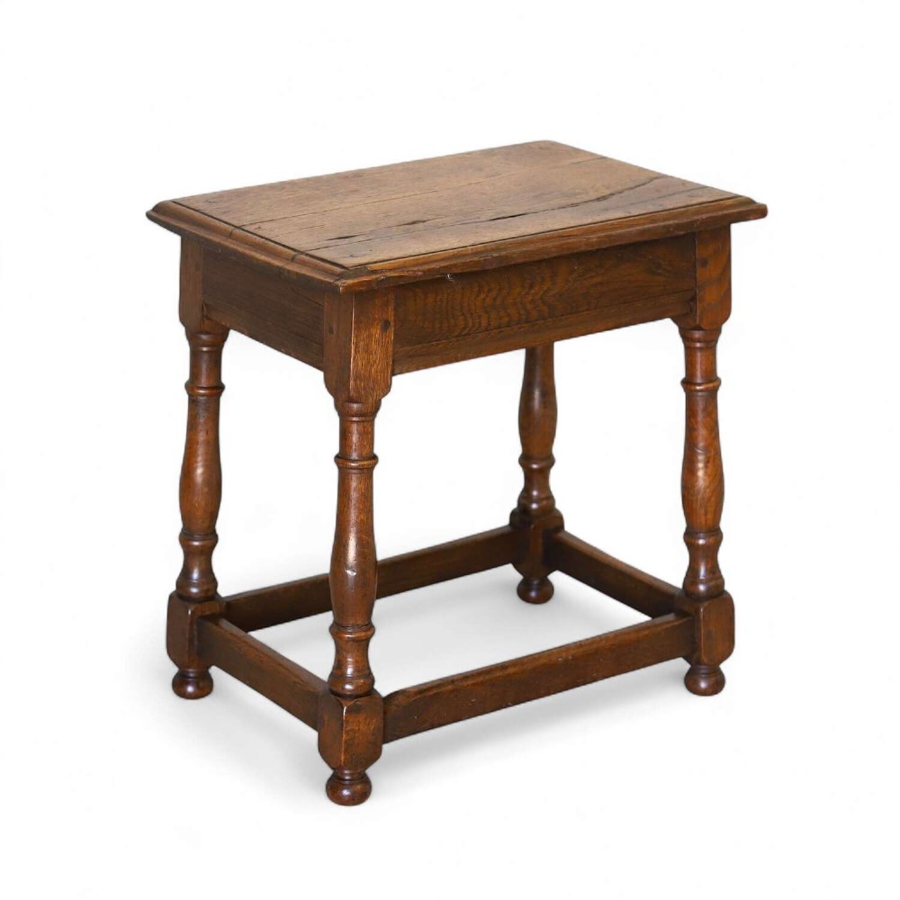 An 18th-century English Georgian oak joint stool featuring turned legs, perimeter stretchers, and a rectangular top with pegged joinery.