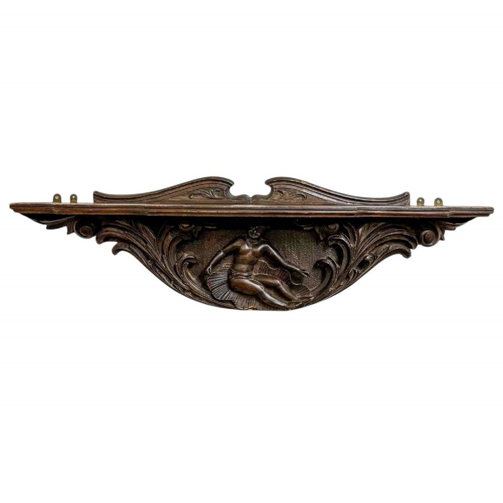 A dark oak wall shelf featuring detailed relief carvings of a central figure flanked by foliate scrollwork.