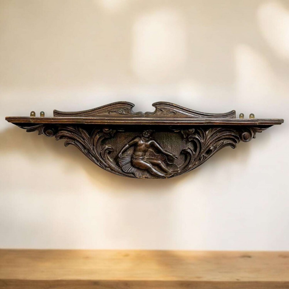 A dark oak wall shelf featuring detailed relief carvings of a central figure flanked by foliate scrollwork. View II