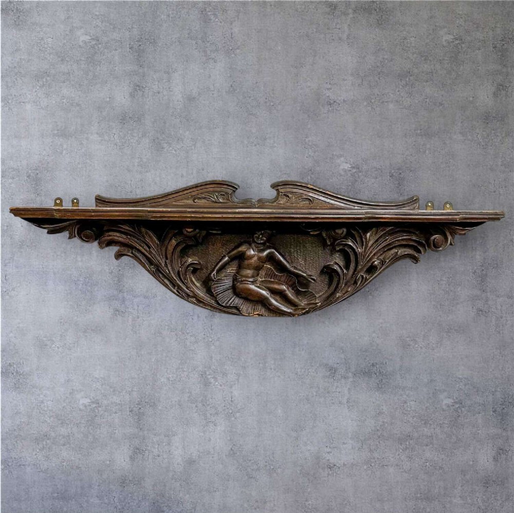 A dark oak wall shelf featuring detailed relief carvings of a central figure flanked by foliate scrollwork. View III