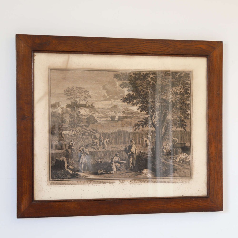 A framed monochrome engraving depicting a classical harvest landscape scene with figures working in a field beneath trees, enclosed in a dark wood frame. View III