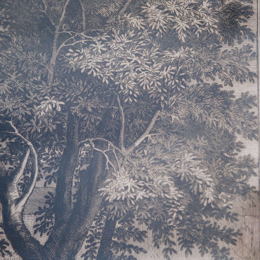 A framed monochrome engraving depicting a classical harvest landscape scene with figures working in a field beneath trees, enclosed in a dark wood frame. View X