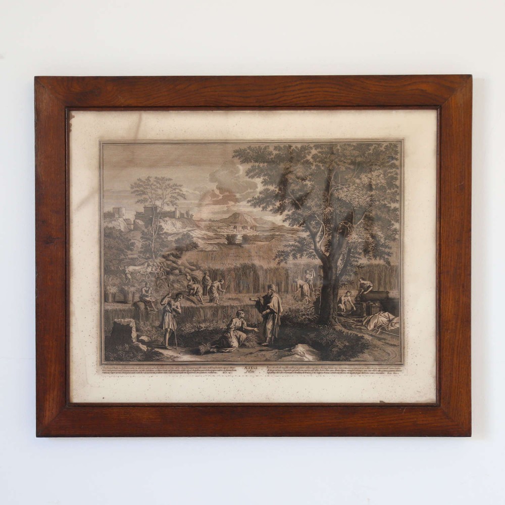A framed monochrome engraving depicting a classical harvest landscape scene with figures working in a field beneath trees, enclosed in a dark wood frame. View XII