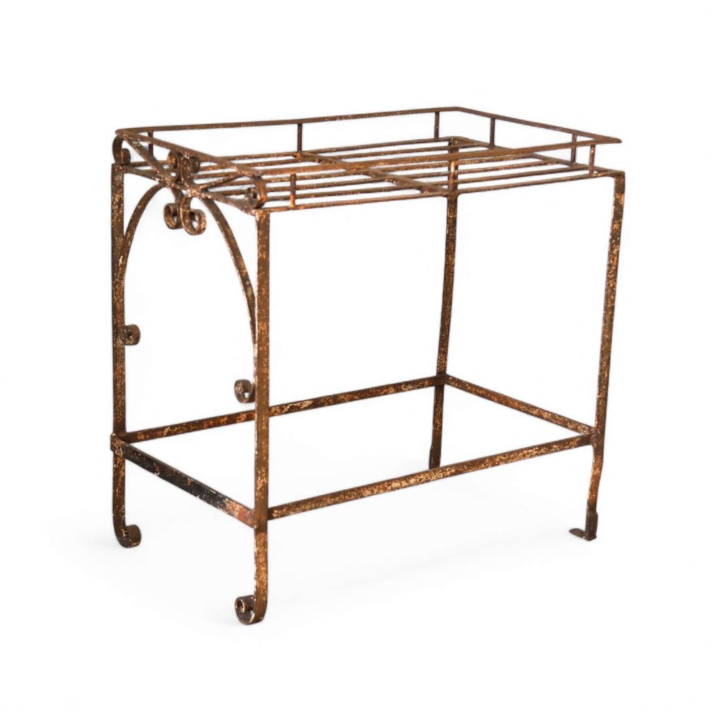A rectangular wrought iron garden rack with a slatted top, decorative side scrollwork, and a weathered brown finish.