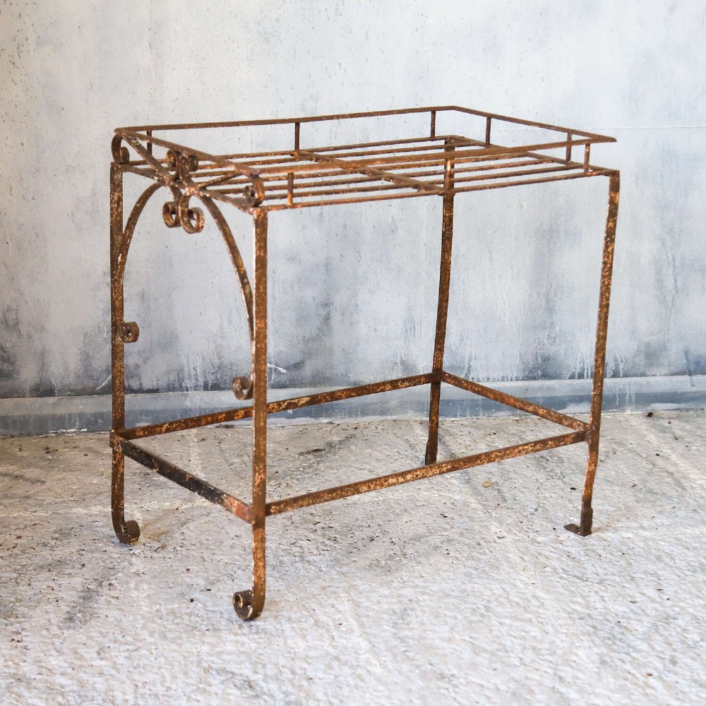 A rectangular wrought iron garden rack with a slatted top, decorative side scrollwork, and a weathered brown finish. View IV