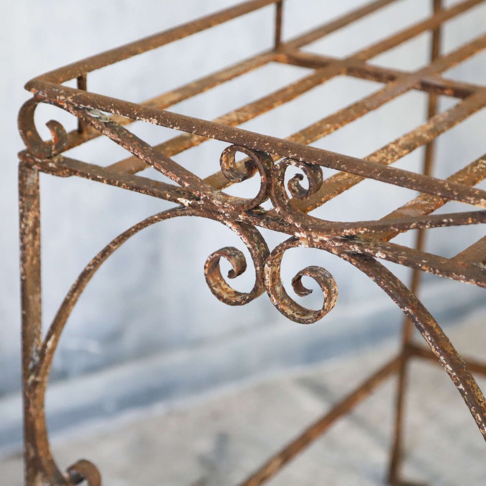A rectangular wrought iron garden rack with a slatted top, decorative side scrollwork, and a weathered brown finish. View V