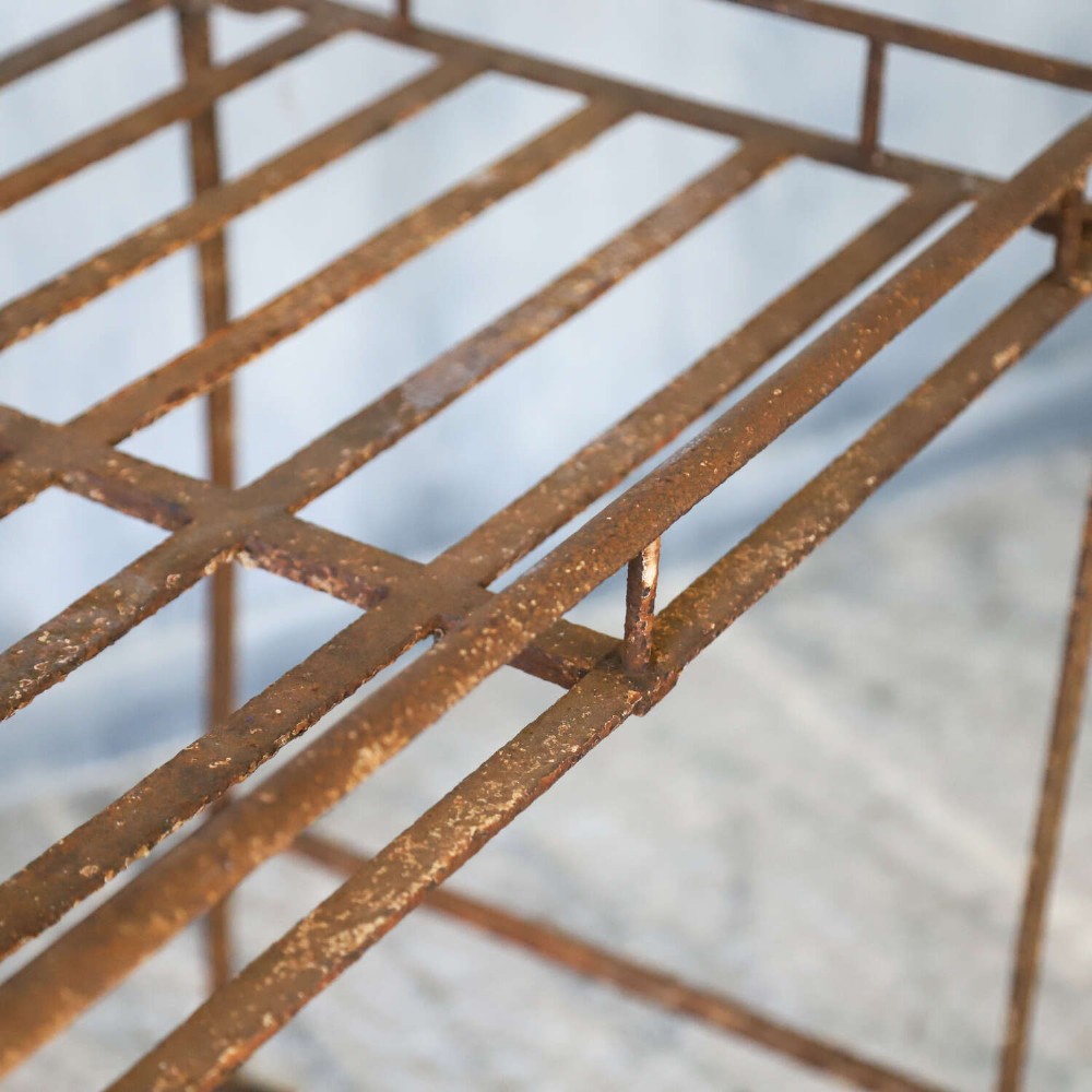A rectangular wrought iron garden rack with a slatted top, decorative side scrollwork, and a weathered brown finish. View VII