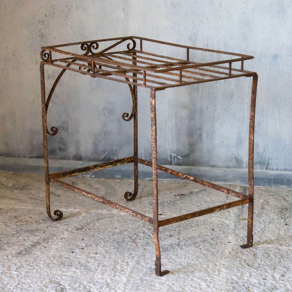 A rectangular wrought iron garden rack with a slatted top, decorative side scrollwork, and a weathered brown finish. View IX