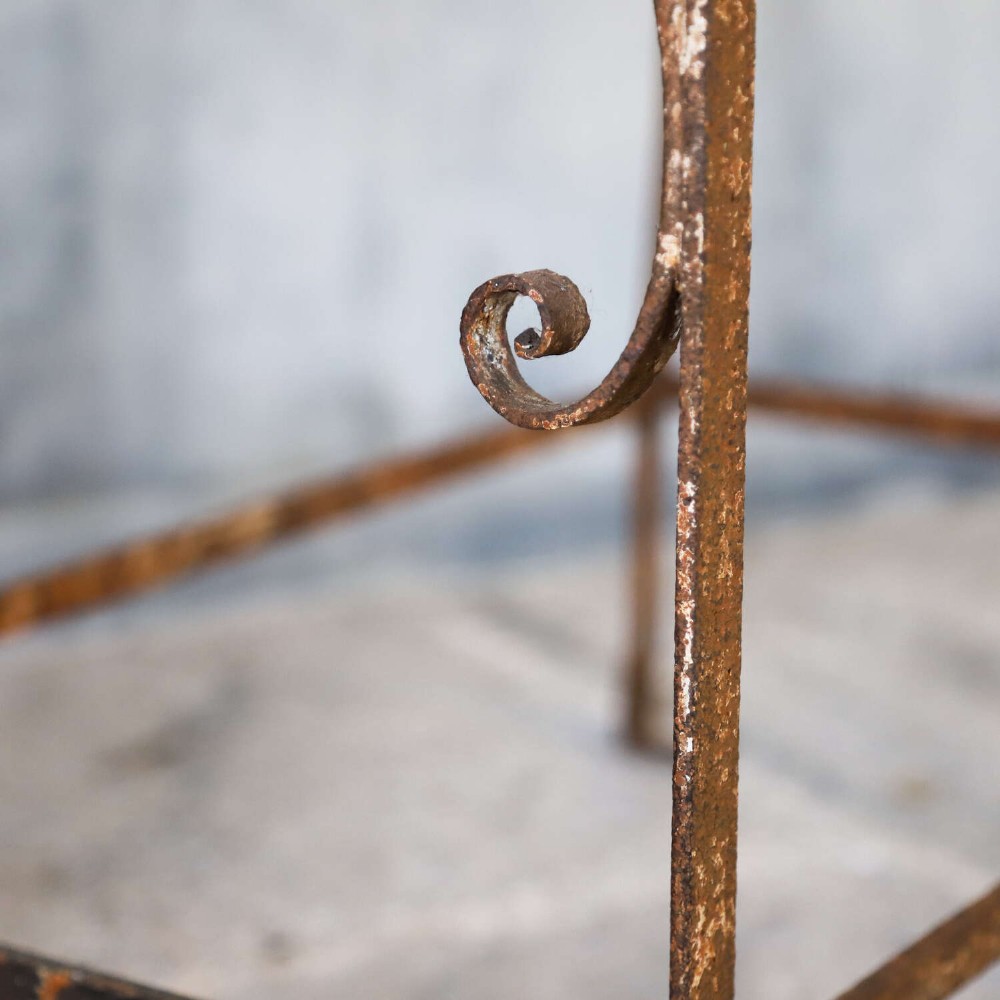 A rectangular wrought iron garden rack with a slatted top, decorative side scrollwork, and a weathered brown finish. View X