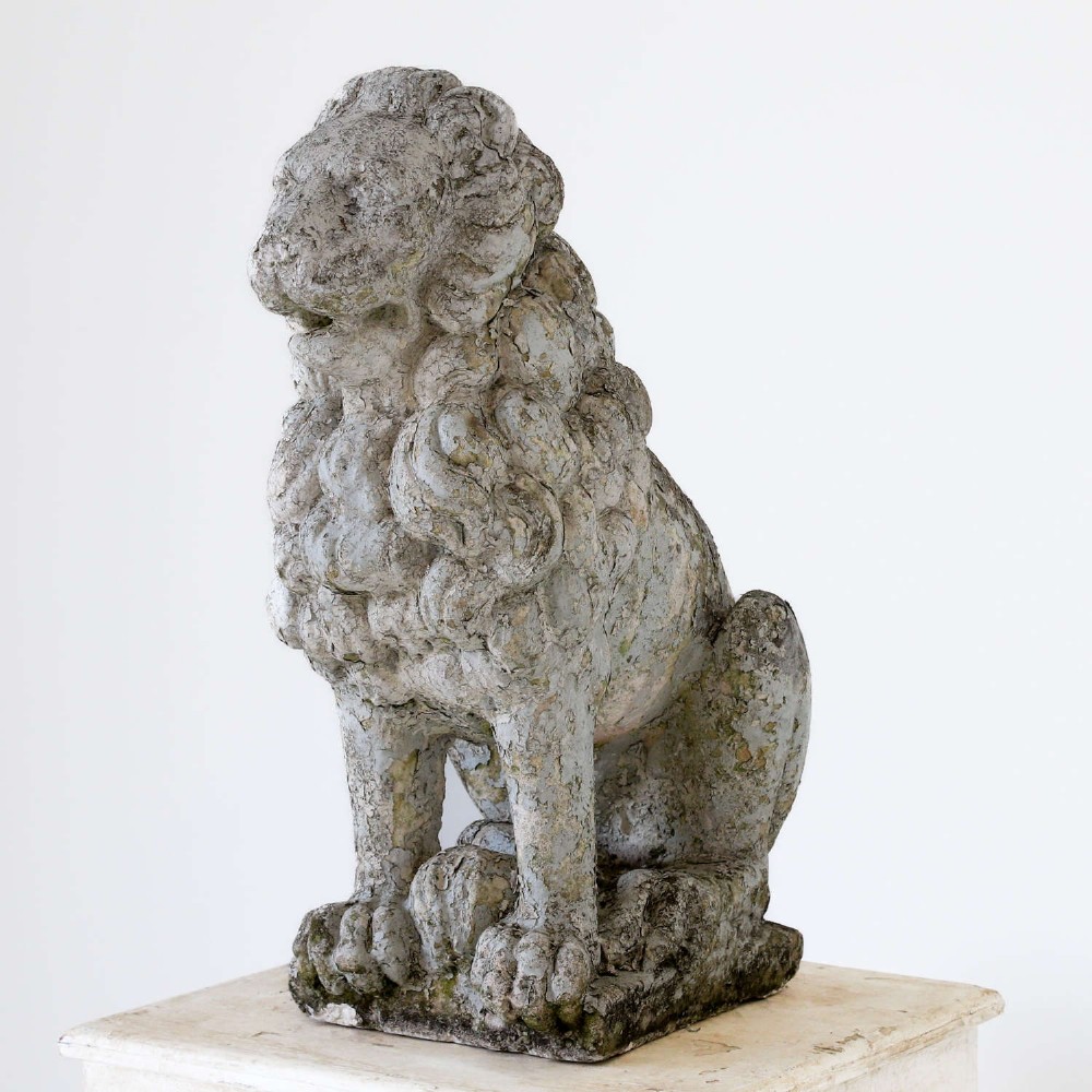 A weathered composite stone statue depicting a seated lion with a distressed, flaking grey paint finish.