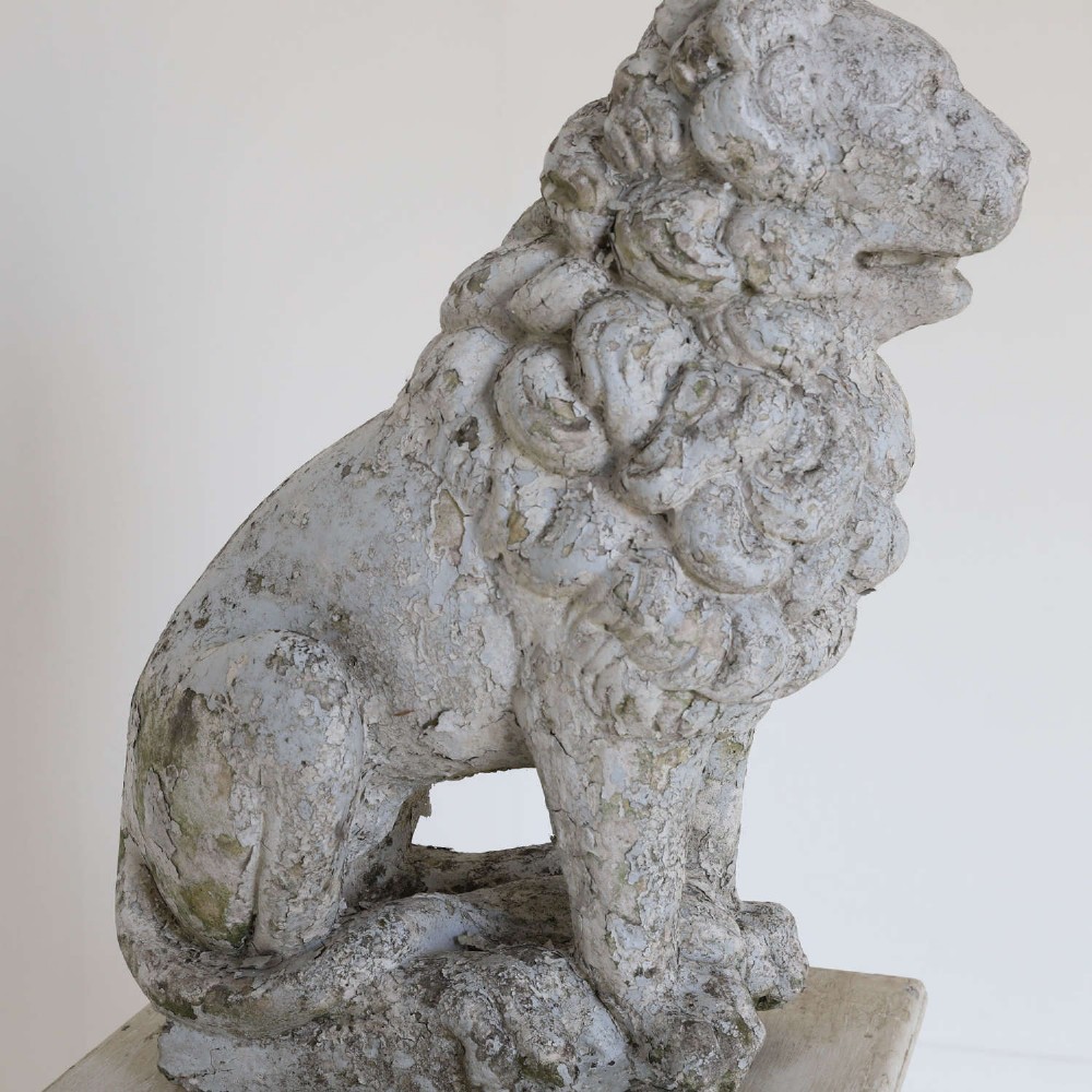 A weathered composite stone statue depicting a seated lion with a distressed, flaking grey paint finish. View IV