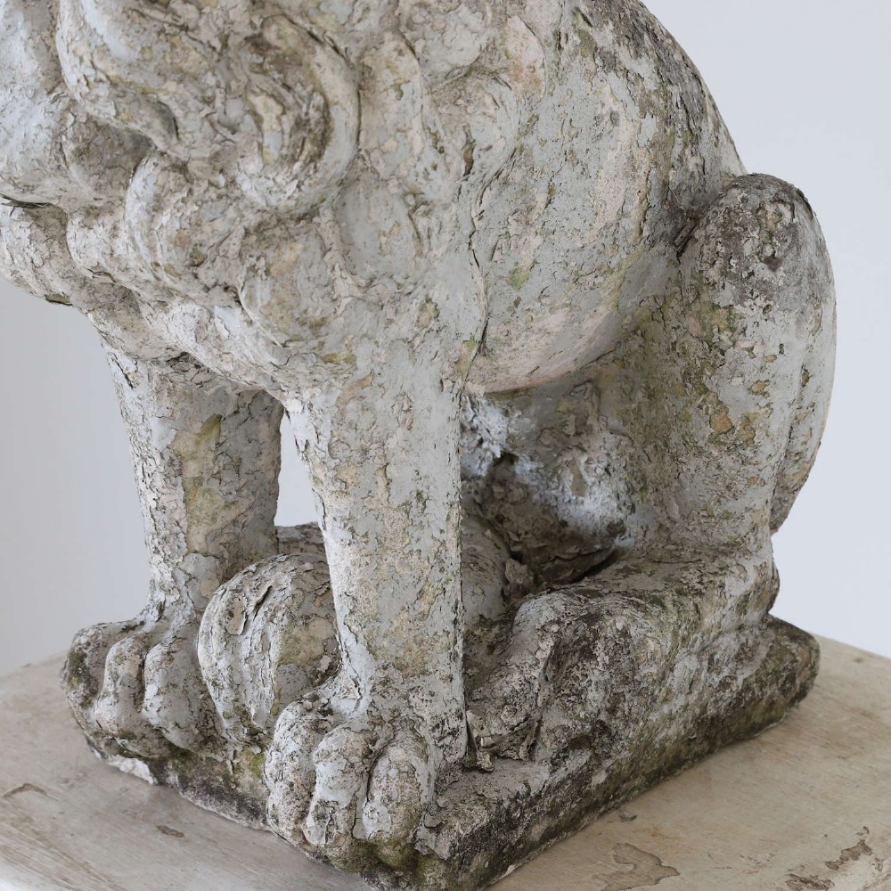 A weathered composite stone statue depicting a seated lion with a distressed, flaking grey paint finish. View V