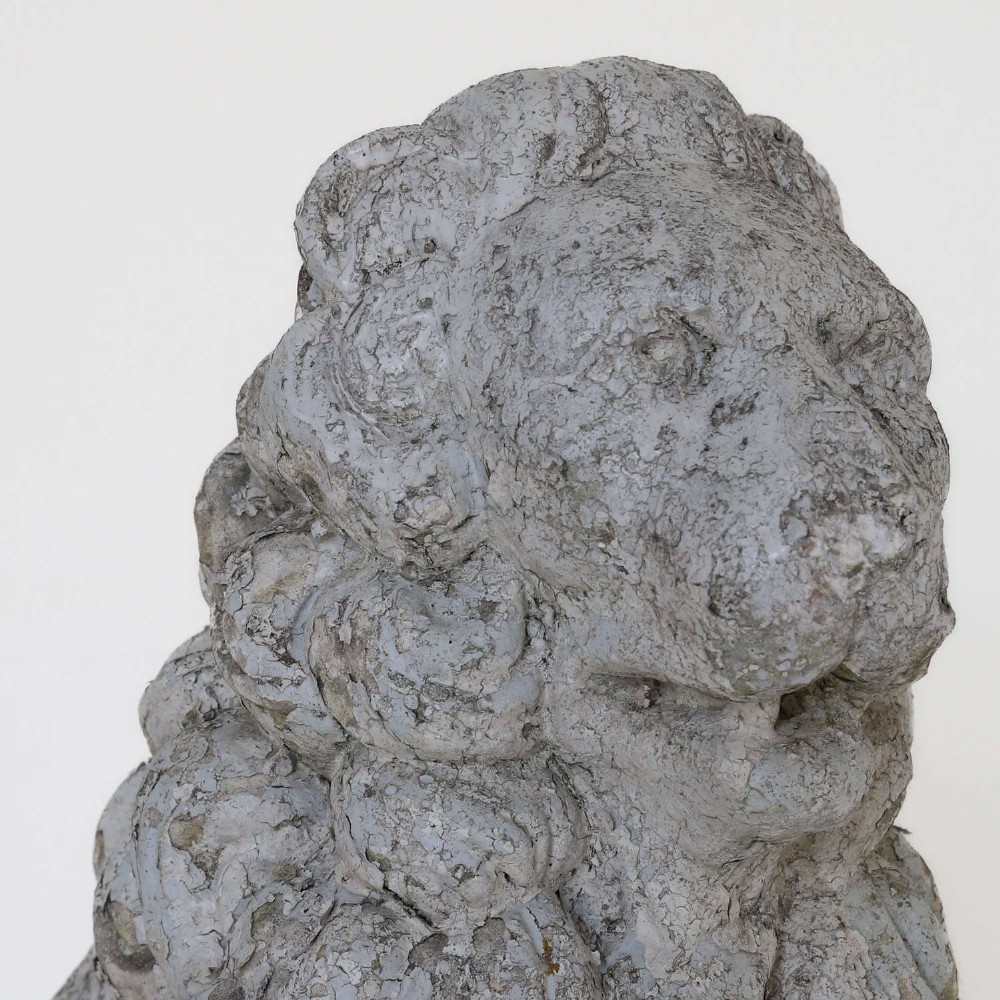 A weathered composite stone statue depicting a seated lion with a distressed, flaking grey paint finish. View VII