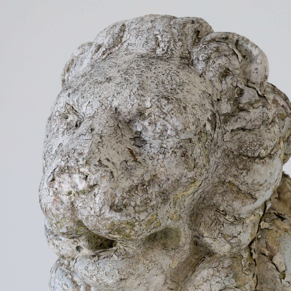 A weathered composite stone statue depicting a seated lion with a distressed, flaking grey paint finish. View VIII