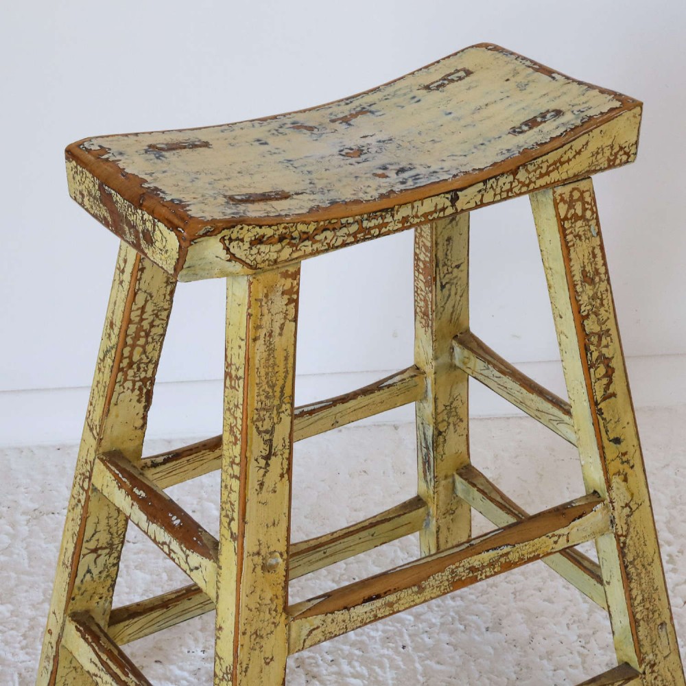 An antique Chinese elm stool featuring a slightly curved seat and a heavily distressed yellow lacquered finish over four splayed legs with horizontal stretchers. View III
