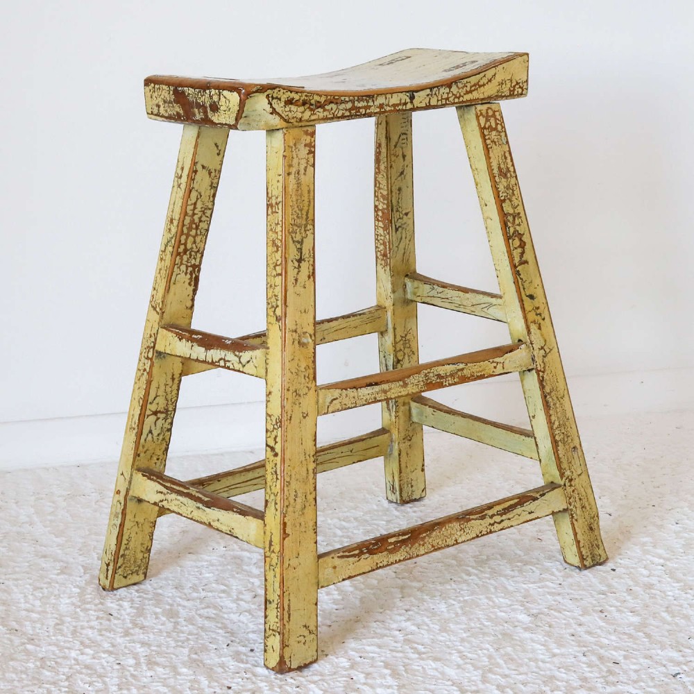 An antique Chinese elm stool featuring a slightly curved seat and a heavily distressed yellow lacquered finish over four splayed legs with horizontal stretchers. View IV