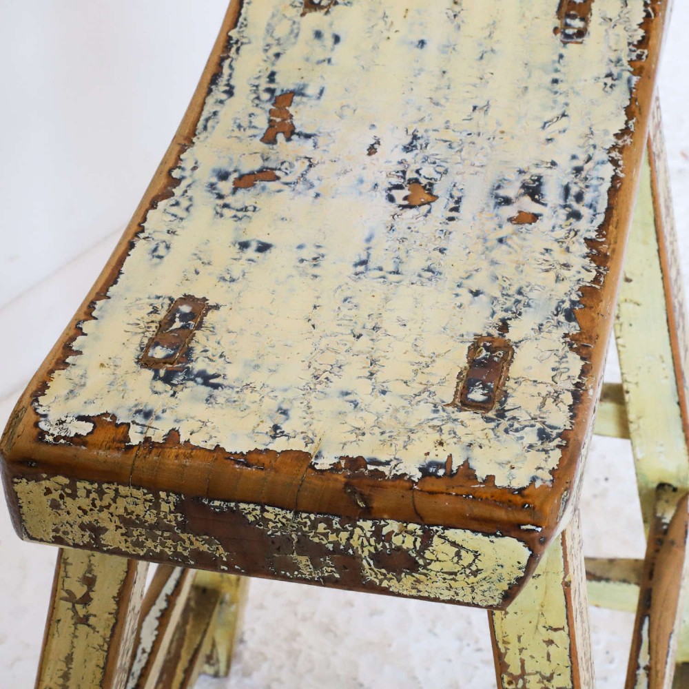 An antique Chinese elm stool featuring a slightly curved seat and a heavily distressed yellow lacquered finish over four splayed legs with horizontal stretchers. View VI