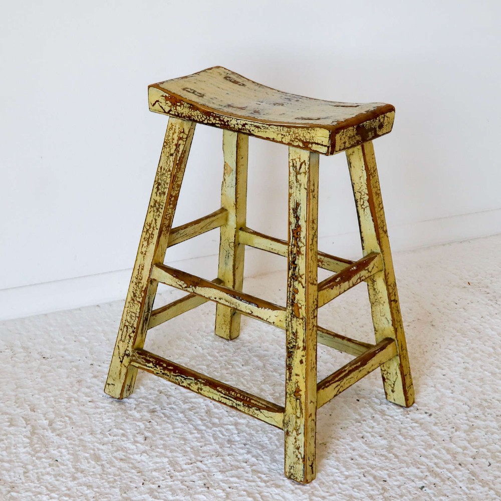 An antique Chinese elm stool featuring a slightly curved seat and a heavily distressed yellow lacquered finish over four splayed legs with horizontal stretchers. View VII