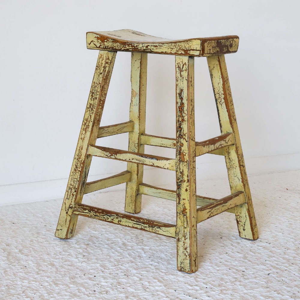 An antique Chinese elm stool featuring a slightly curved seat and a heavily distressed yellow lacquered finish over four splayed legs with horizontal stretchers. View VIII
