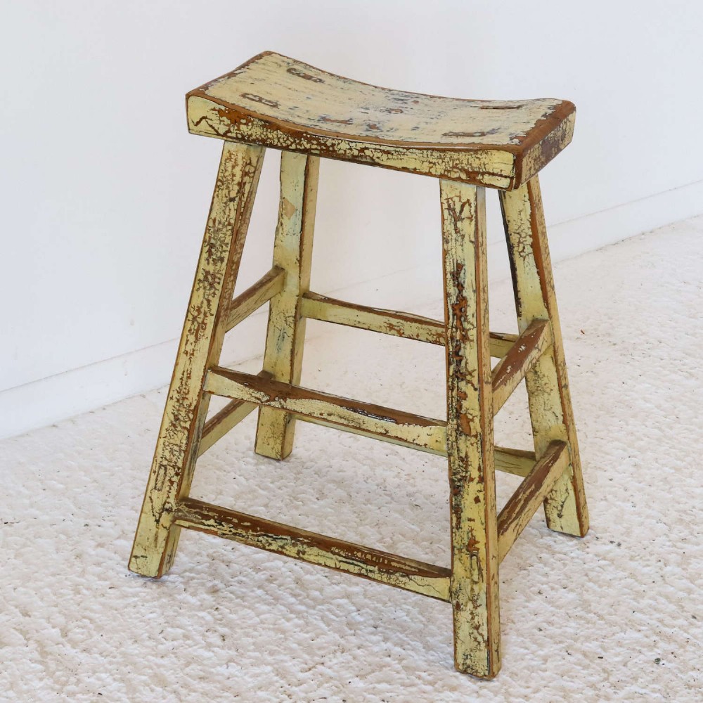 An antique Chinese elm stool featuring a slightly curved seat and a heavily distressed yellow lacquered finish over four splayed legs with horizontal stretchers. View IX