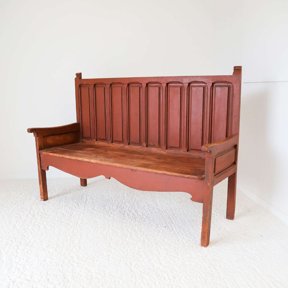 A late nineteenth-century Spanish wooden settle bench with a terracotta red painted frame, tall panelled backrest, shaped apron, and a natural timber seat.