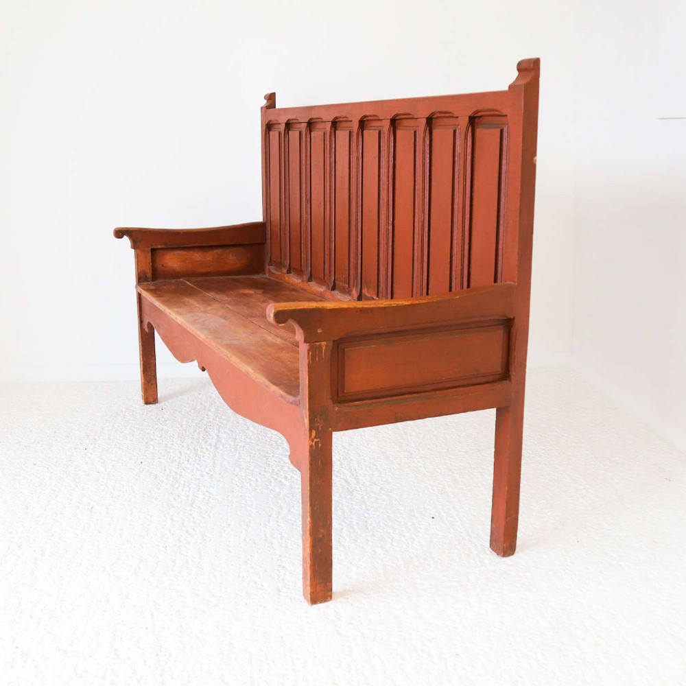 A late nineteenth-century Spanish wooden settle bench with a terracotta red painted frame, tall panelled backrest, shaped apron, and a natural timber seat. View II