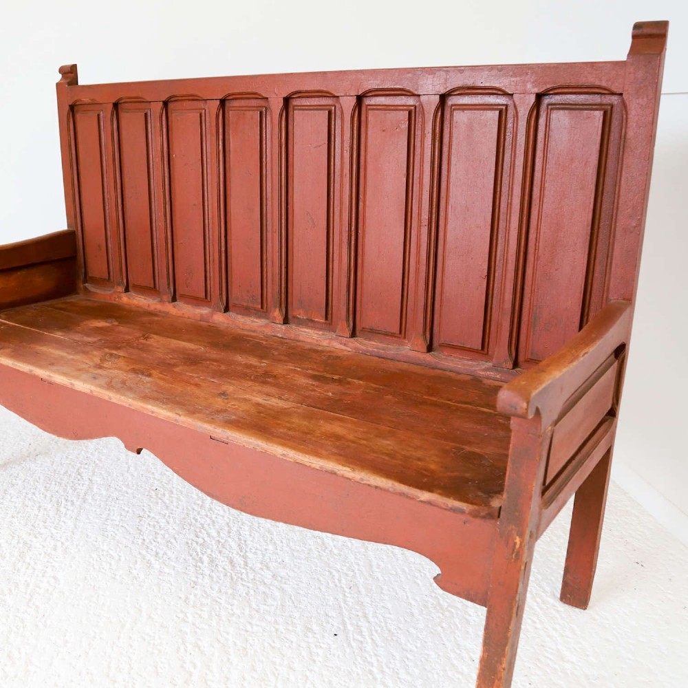 A late nineteenth-century Spanish wooden settle bench with a terracotta red painted frame, tall panelled backrest, shaped apron, and a natural timber seat. View III