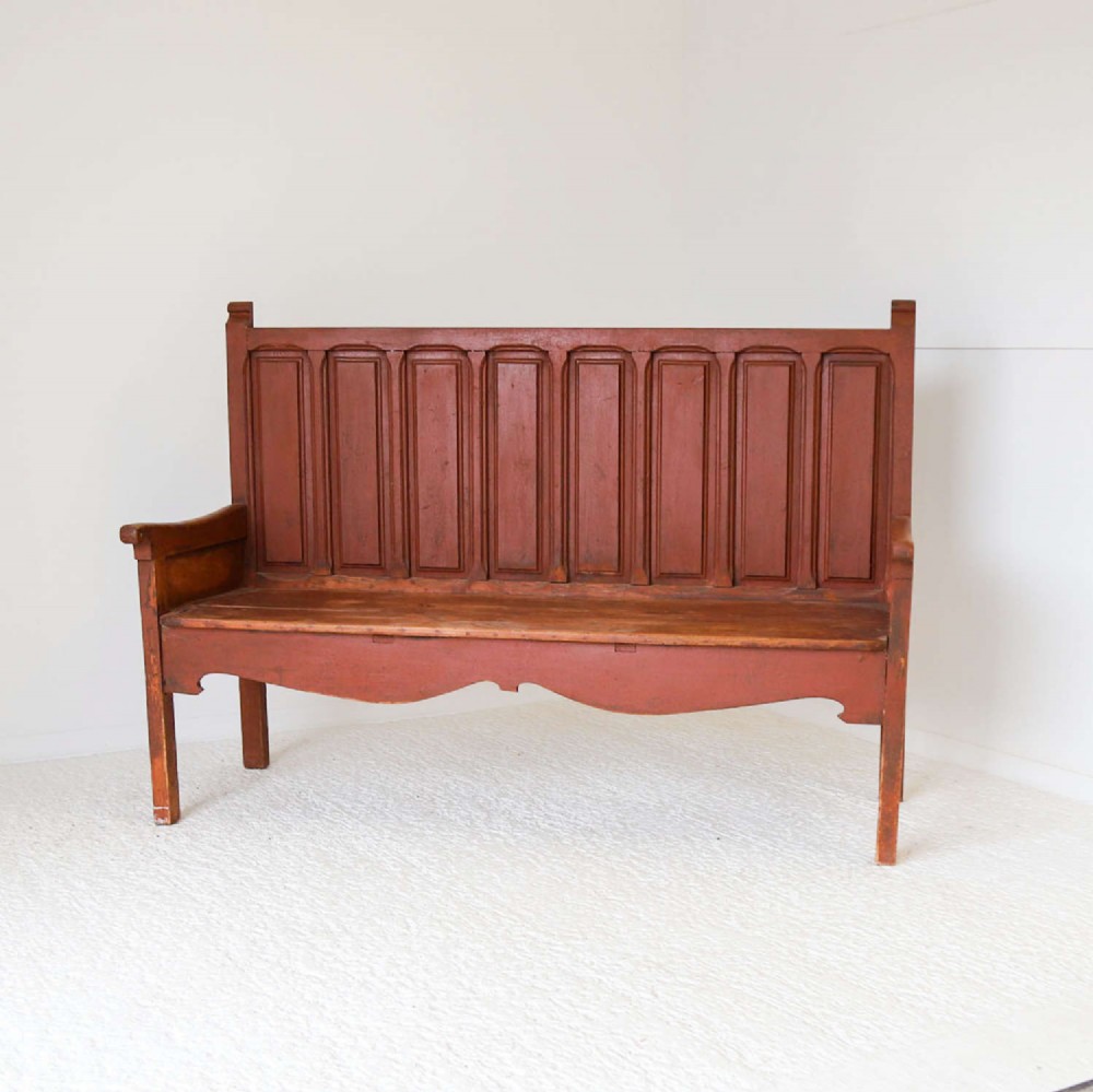 A late nineteenth-century Spanish wooden settle bench with a terracotta red painted frame, tall panelled backrest, shaped apron, and a natural timber seat. View IV