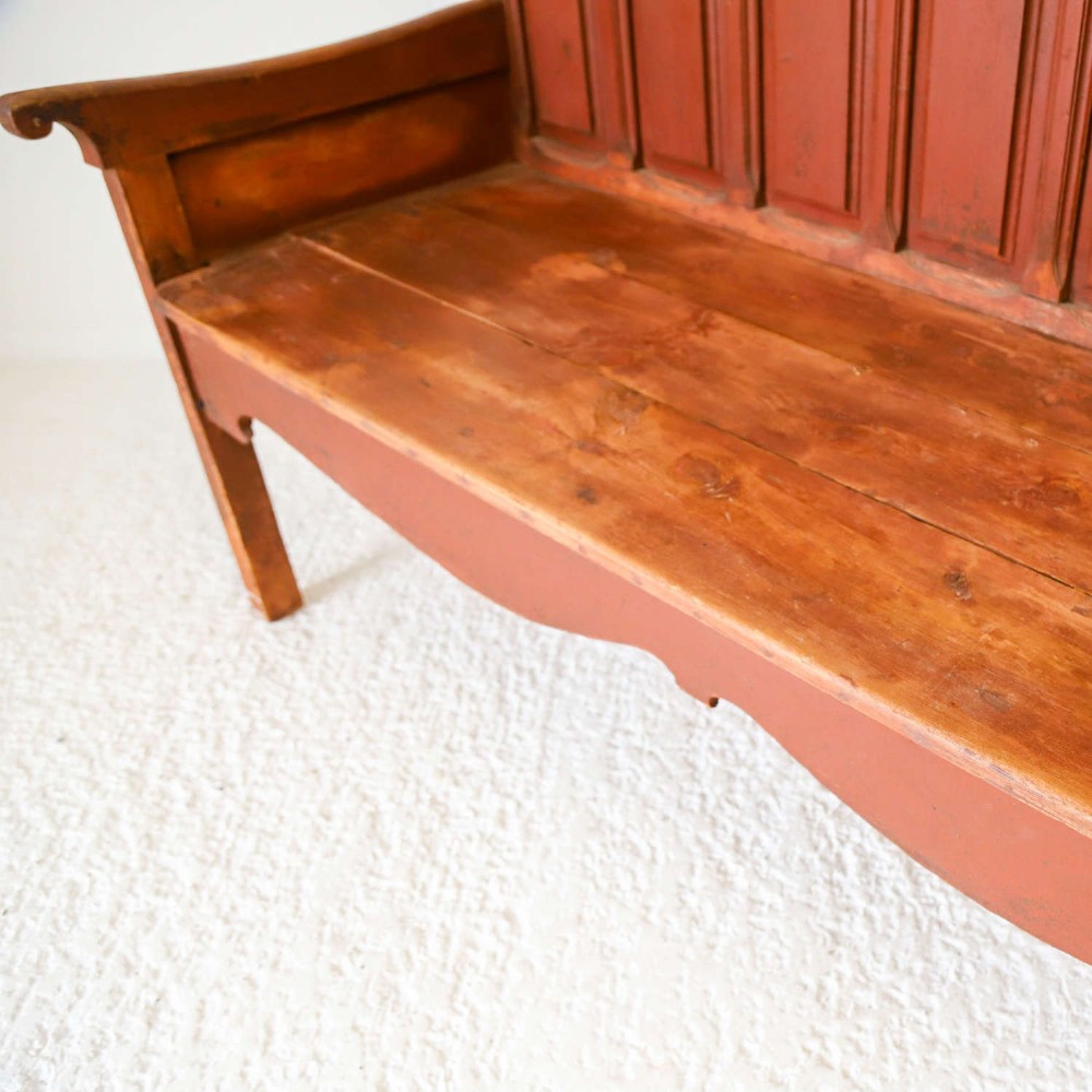 A late nineteenth-century Spanish wooden settle bench with a terracotta red painted frame, tall panelled backrest, shaped apron, and a natural timber seat. View VII