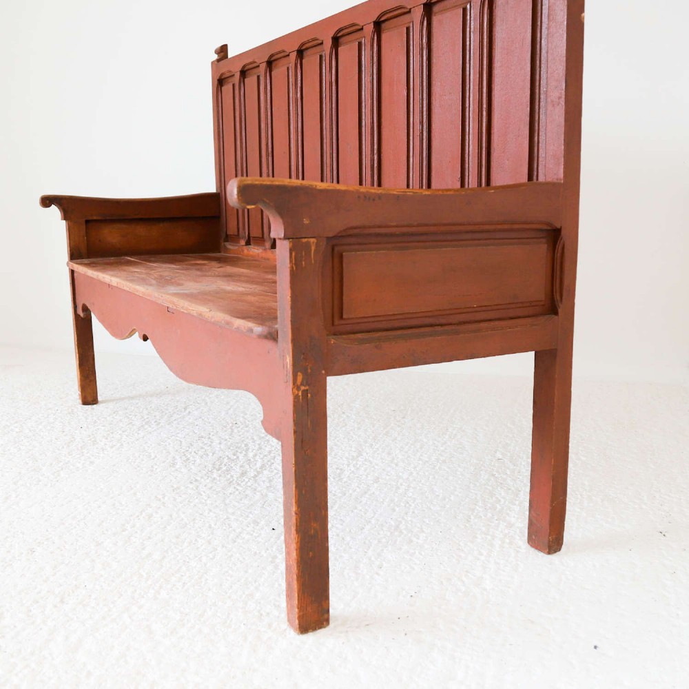 A late nineteenth-century Spanish wooden settle bench with a terracotta red painted frame, tall panelled backrest, shaped apron, and a natural timber seat. View X