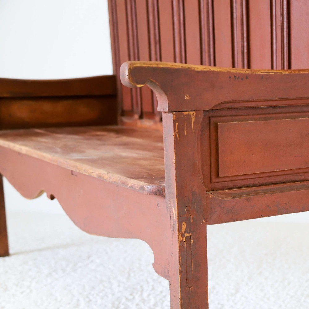 A late nineteenth-century Spanish wooden settle bench with a terracotta red painted frame, tall panelled backrest, shaped apron, and a natural timber seat. View XI