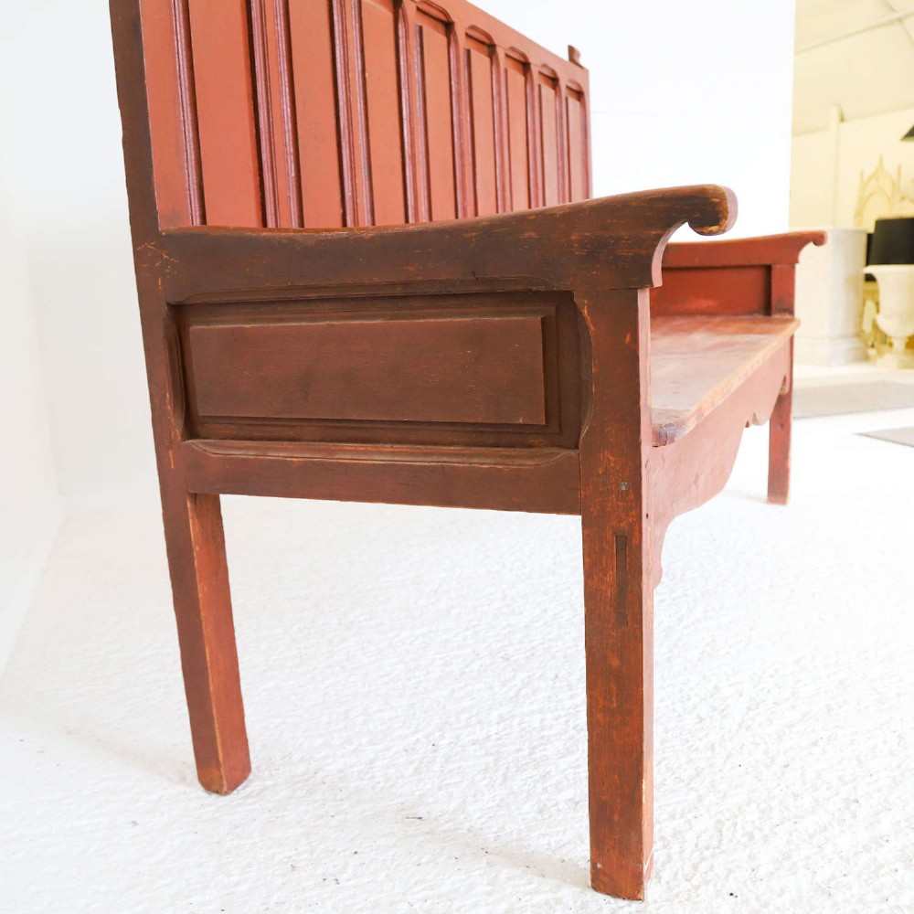 A late nineteenth-century Spanish wooden settle bench with a terracotta red painted frame, tall panelled backrest, shaped apron, and a natural timber seat. View XIV