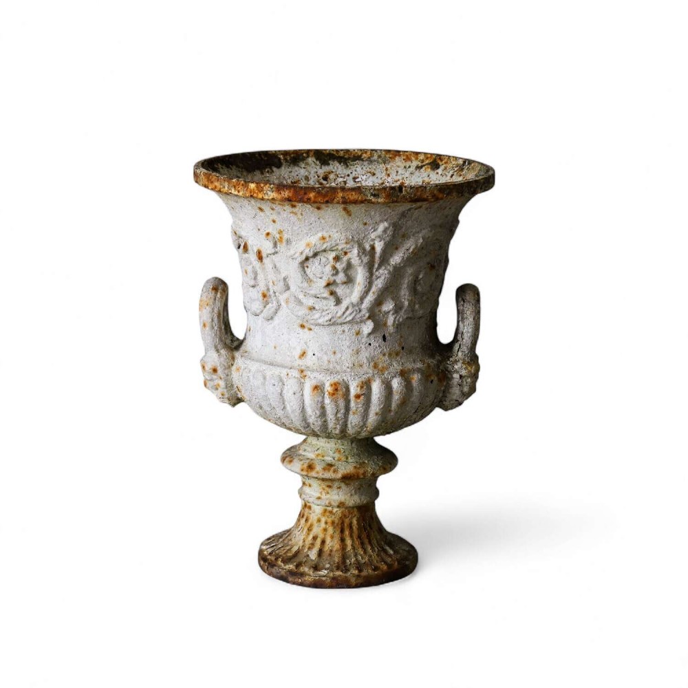 A Victorian weathered white cast iron Campana urn with twin loop handles, floral relief moulding, and surface rust.