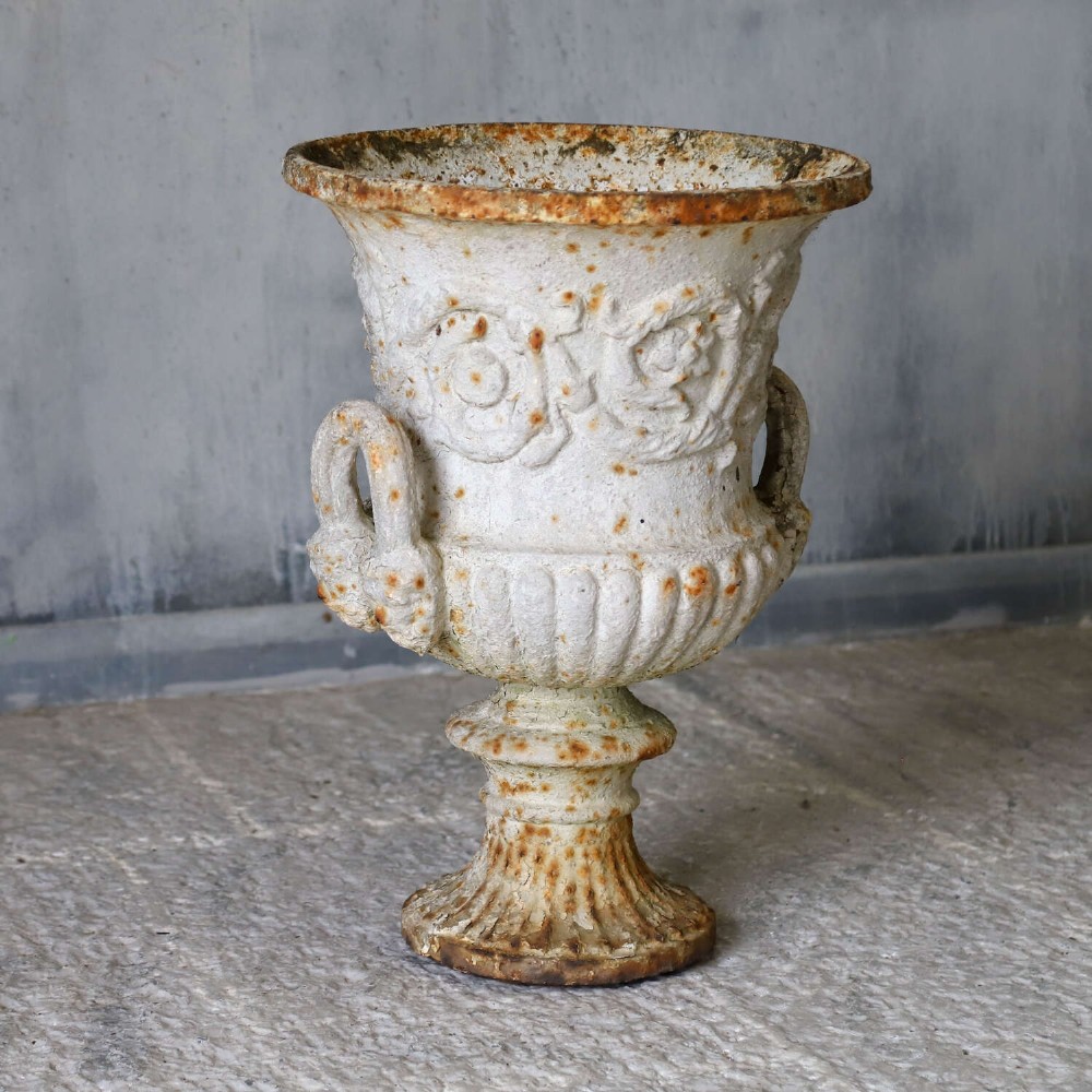 A Victorian weathered white cast iron Campana urn with twin loop handles, floral relief moulding, and surface rust. View III
