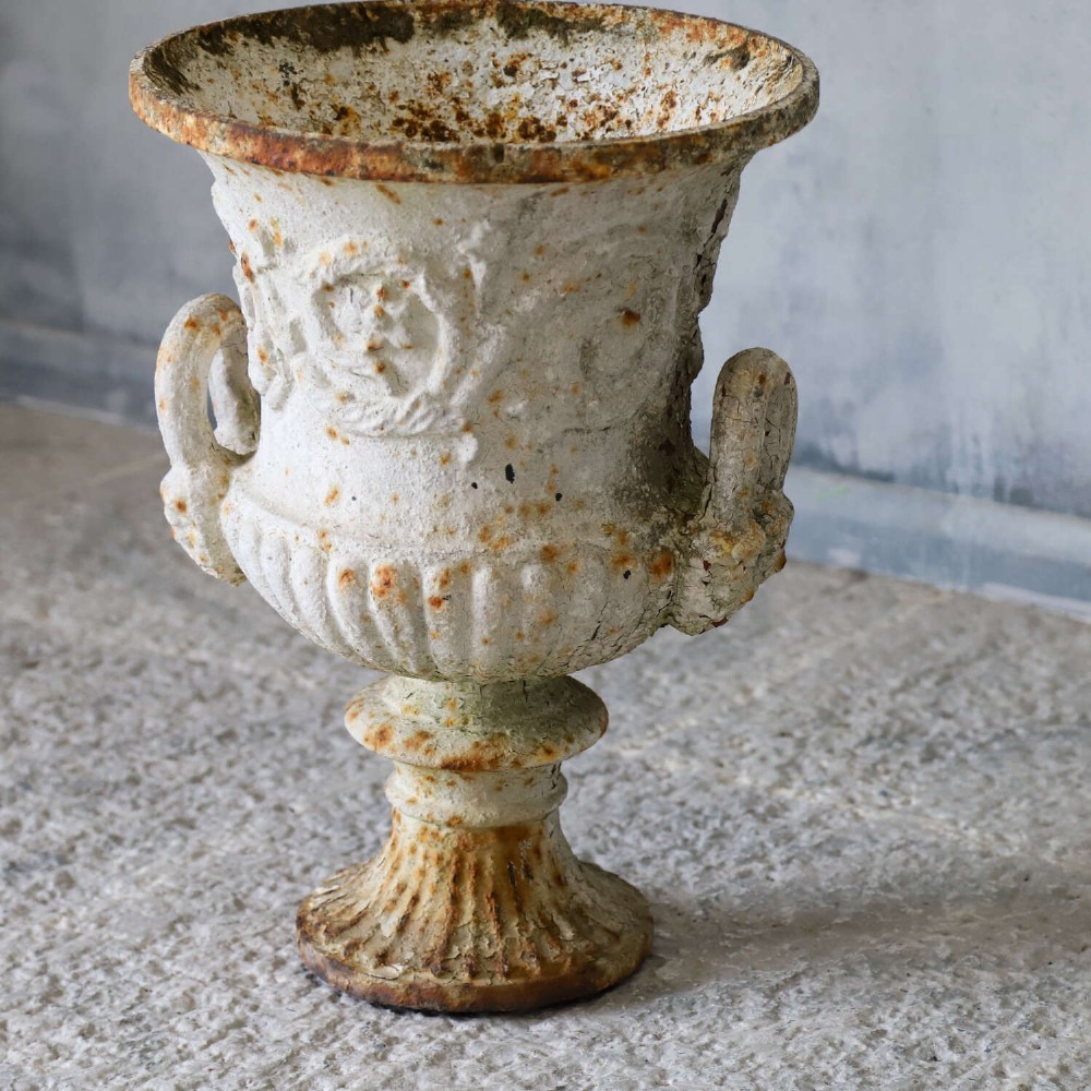 A Victorian weathered white cast iron Campana urn with twin loop handles, floral relief moulding, and surface rust. View IV
