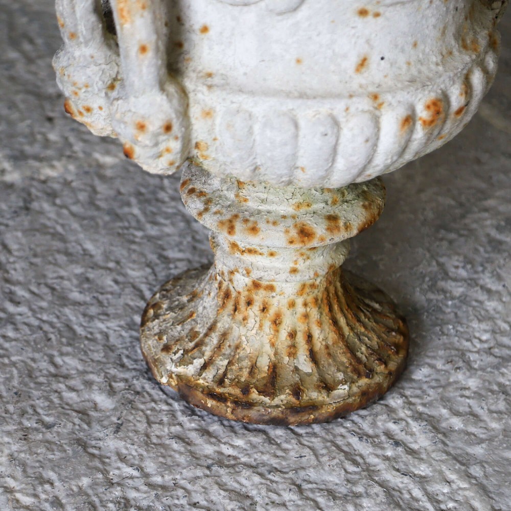 A Victorian weathered white cast iron Campana urn with twin loop handles, floral relief moulding, and surface rust. View V