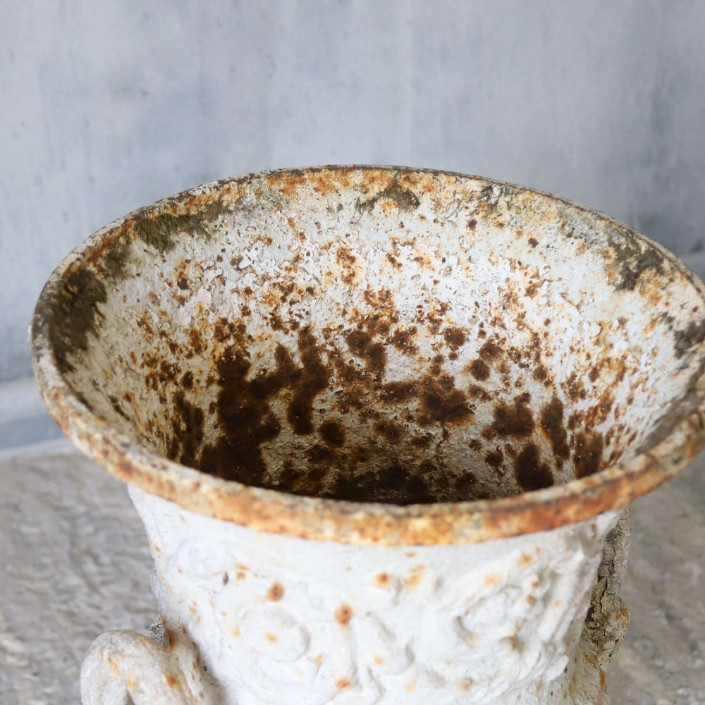 A Victorian weathered white cast iron Campana urn with twin loop handles, floral relief moulding, and surface rust. View VI