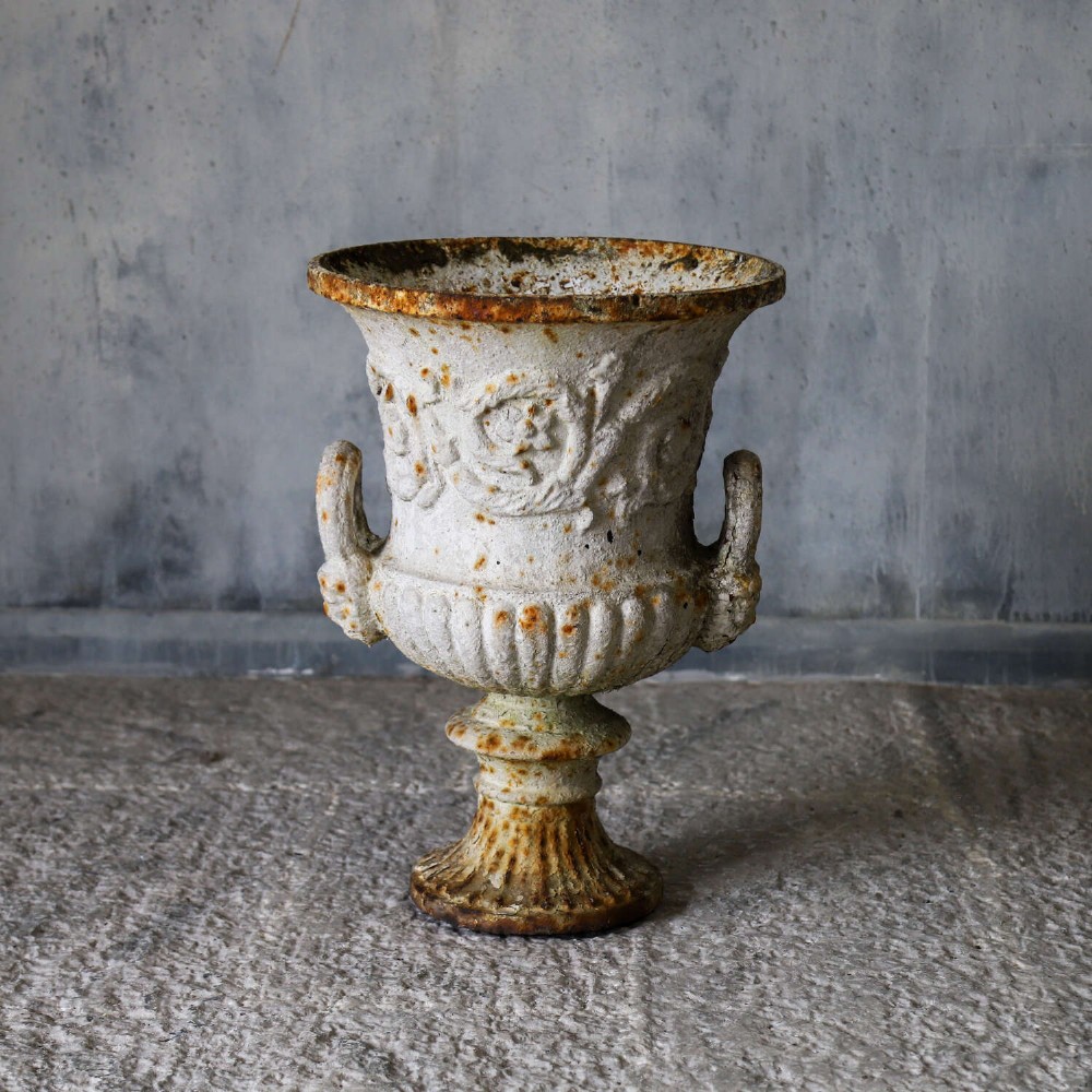 A Victorian weathered white cast iron Campana urn with twin loop handles, floral relief moulding, and surface rust. View VII