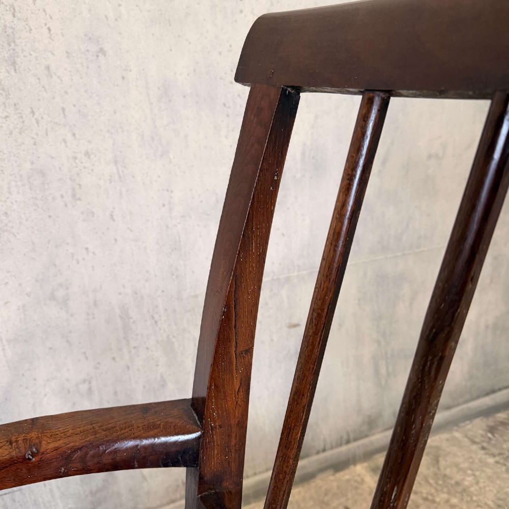 An early Georgian dark oak and walnut commode armchair featuring a vertical slatted back, curved armrests, turned front supports, and a deep enclosed box seat. View IX