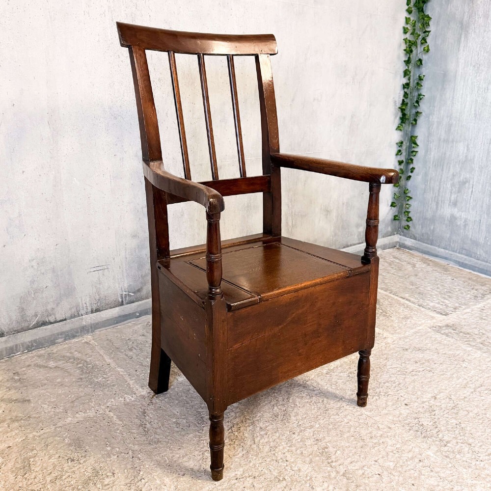 An early Georgian dark oak and walnut commode armchair featuring a vertical slatted back, curved armrests, turned front supports, and a deep enclosed box seat. View XIII