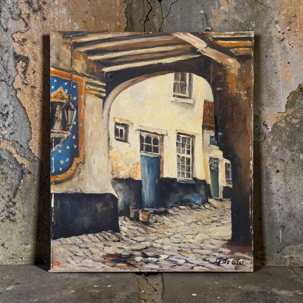 An oil painting on canvas depicting a Flemish cobbled street framed by a dark archway, featuring white plaster buildings and a blue door, signed by L. De Gent. View X
