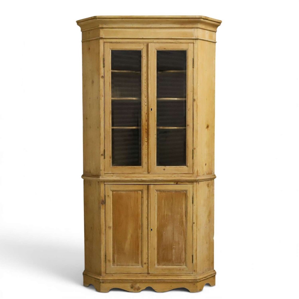 A nineteenth-century two-part pine corner cupboard featuring glazed upper doors and panelled lower doors with a shaped apron.