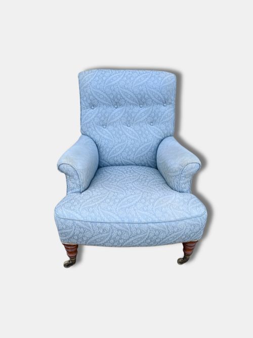 fig 1. A late Victorian Howard and Sons armchair upholstered in light blue paisley fabric, featuring button-tufted backrest detail, rolled arms, and turned wooden front legs with brass castors.