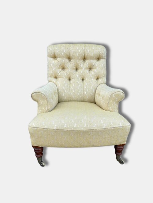 fig 1. A Victorian armchair upholstered in pale yellow patterned fabric featuring a deep-buttoned backrest, scrolled armrests, and turned wood legs with brass castors.