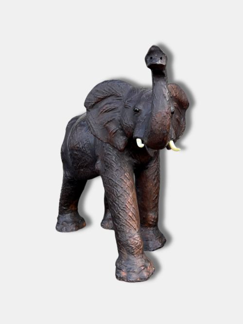 fig 1. An extra-large antique dark brown leather elephant bench featuring a raised trunk, detailed hide texture, glass eyes, and short tusks.