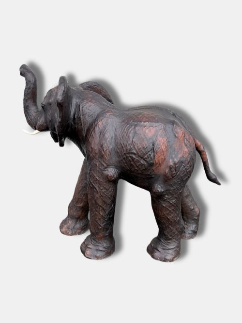fig 2. An extra-large antique dark brown leather elephant bench featuring a raised trunk, detailed hide texture, glass eyes, and short tusks.