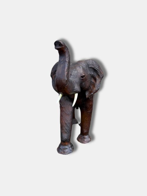 fig 1. A full-grain dark brown leather footstool shaped as an elephant with an upright trunk and white tusks.